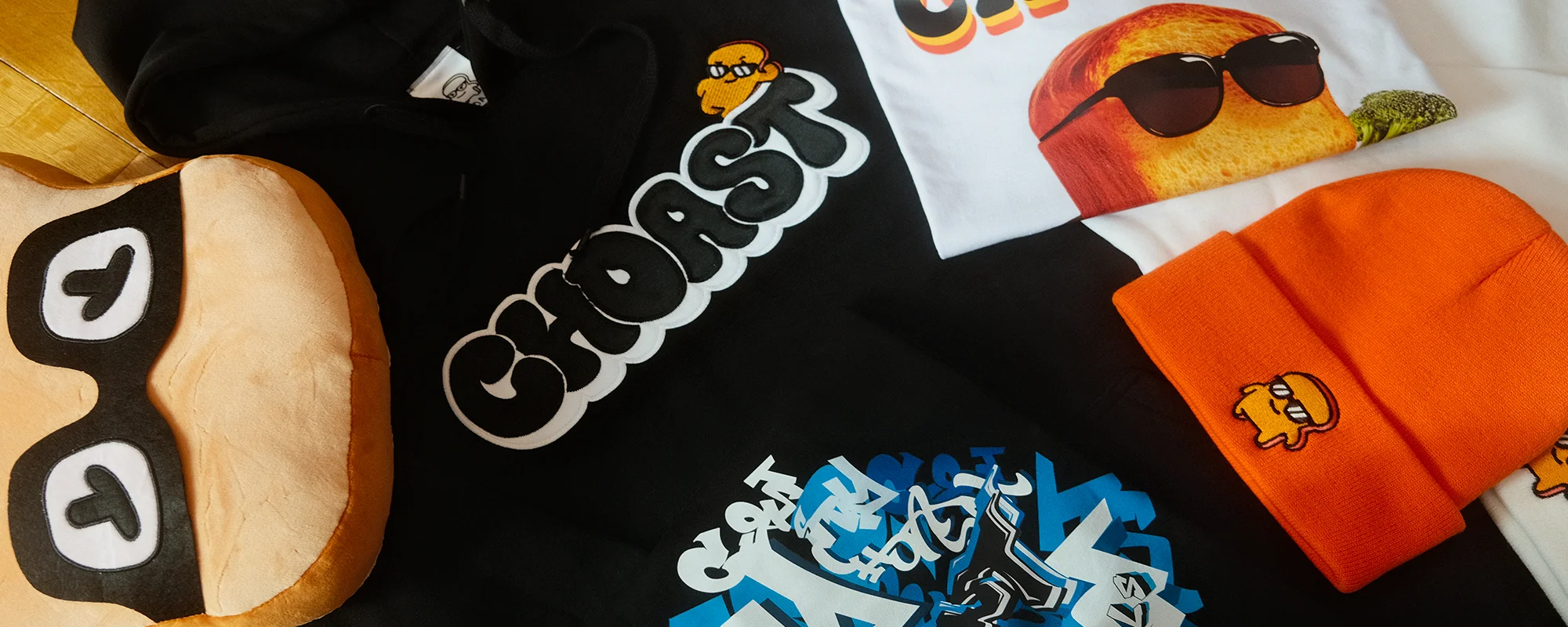 Our choast smoke accessories laying on a colorful beach towel. Showing our different products which are; Choast Plushie, choast bubble hoodie, choast n brocc tee, grafftee, and choast toque.